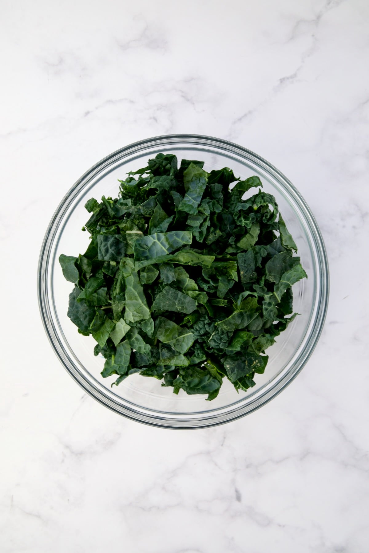 Sliced raw Tuscan kale in glass bowl.