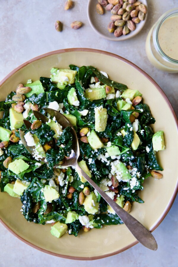 Tuscan Kale Salad with Lemon Tahini Dressing in beige bowl with serving spoon.