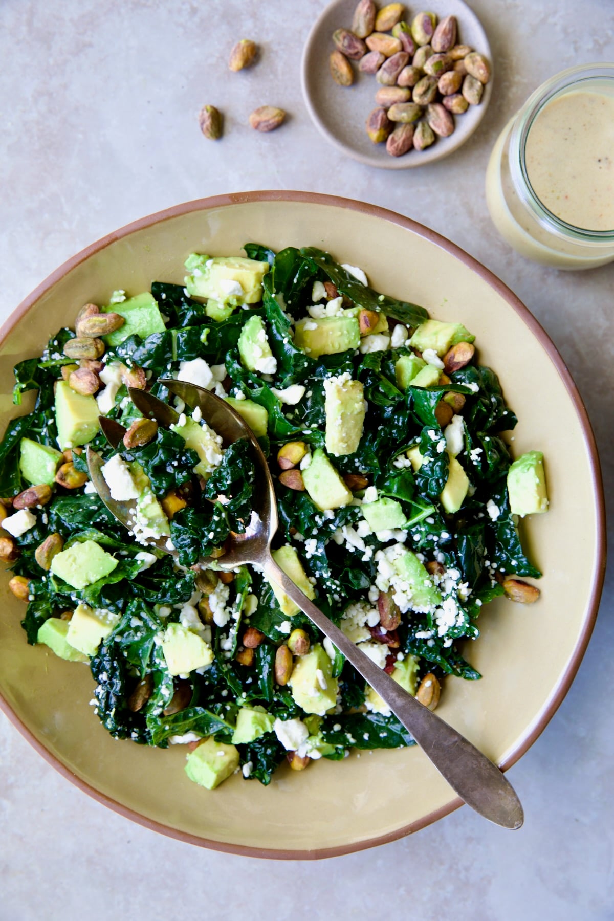 Tuscan Kale Salad with Lemon Tahini Dressing in beige bowl with serving spoon.