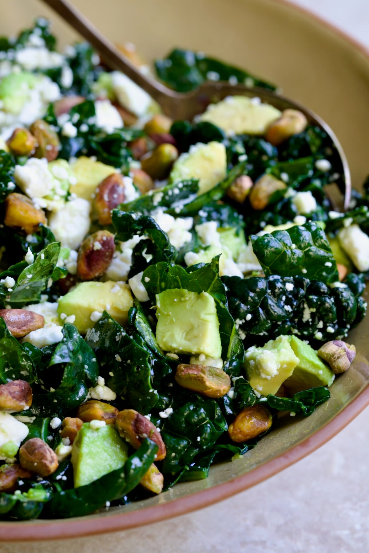 Tuscan Kale Salad with Lemon Tahini Dressing in beige bowl with serving spoon.