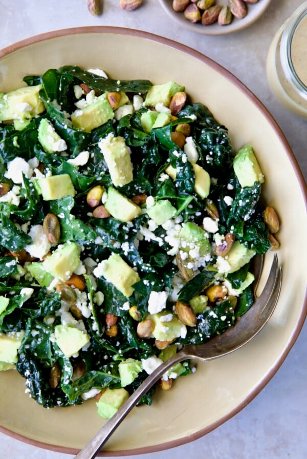 Tuscan Kale Salad with Lemon Tahini Dressing in beige bowl with serving spoon.
