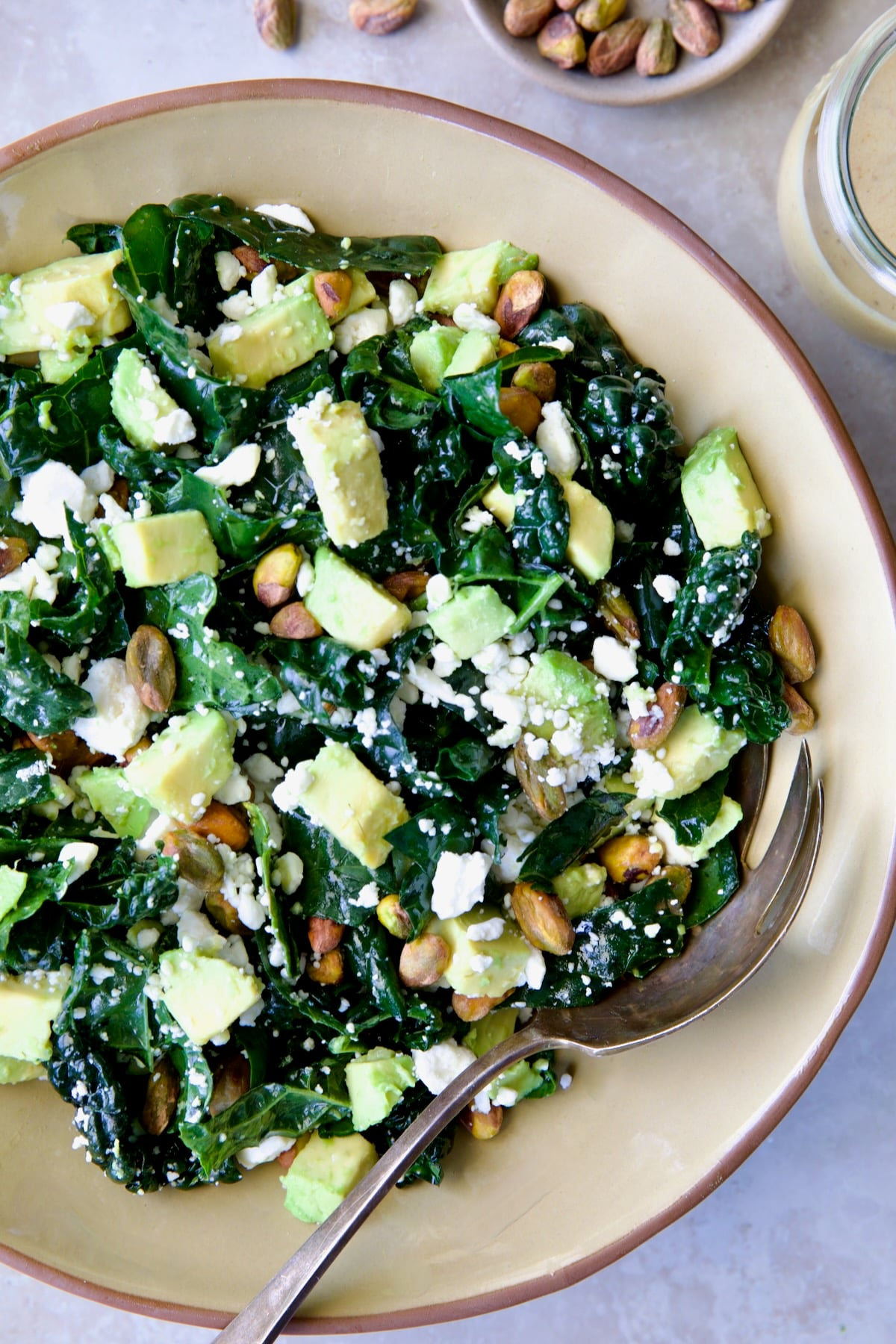 Tuscan Kale Salad with Lemon Tahini Dressing in beige bowl with serving spoon.