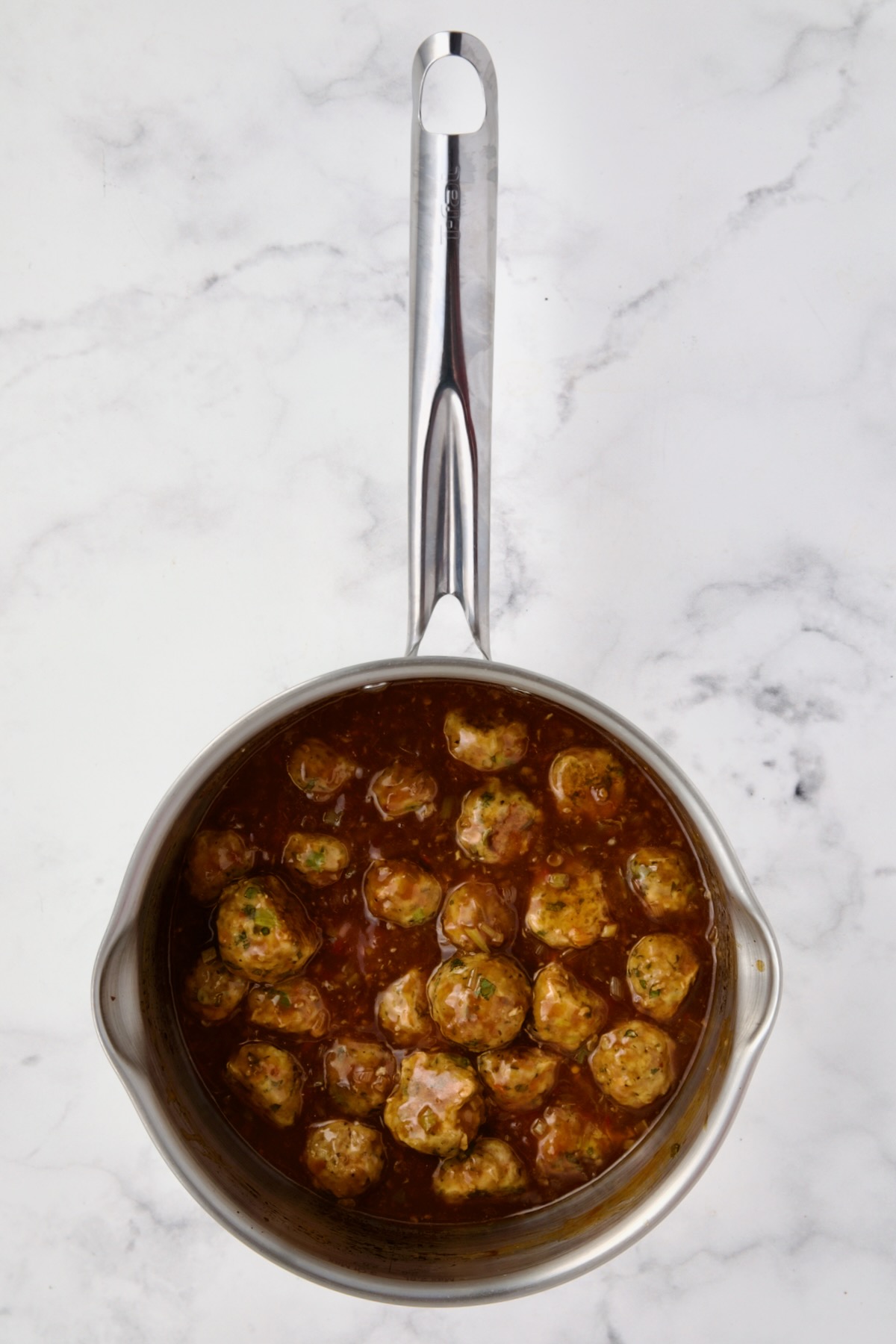 Meatballs and sauce in stainless steel saucepan.