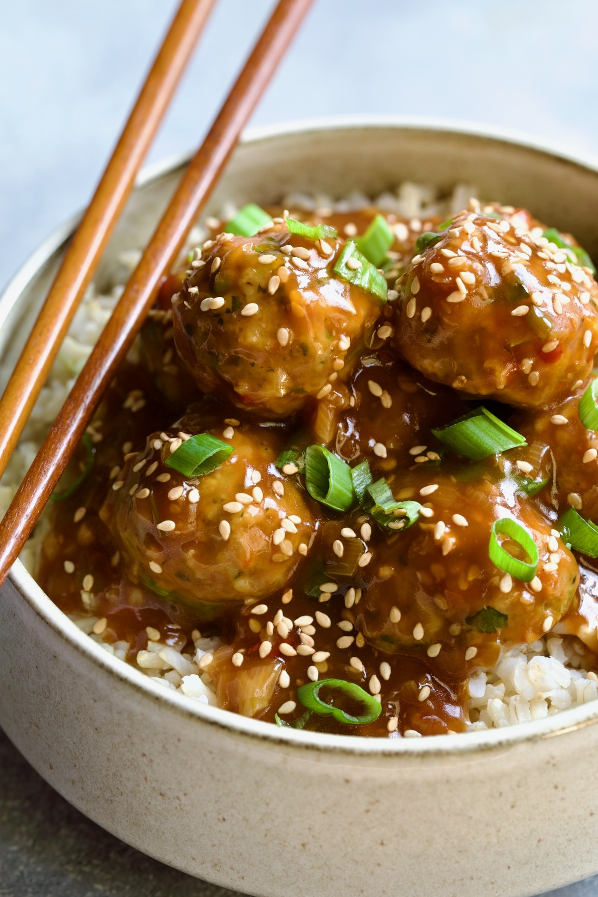 Asian Turkey Meatballs in serving bowl with chopsticks garnished with sesame seeds and scallions over brown rice.