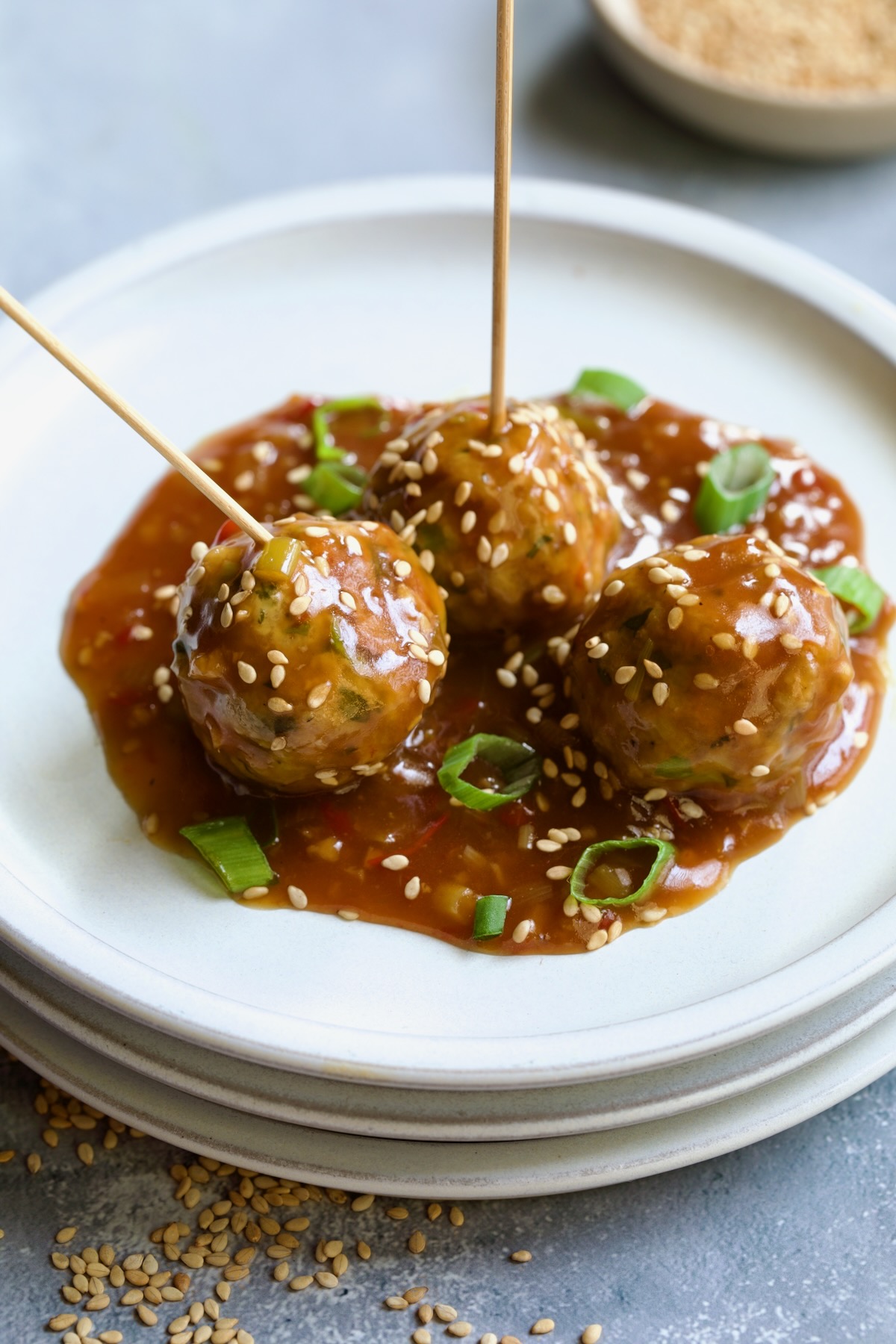 Three Asian Turkey Meatballs on appetizer plates with serving picks inserted garnished with sesame seeds and scallions.