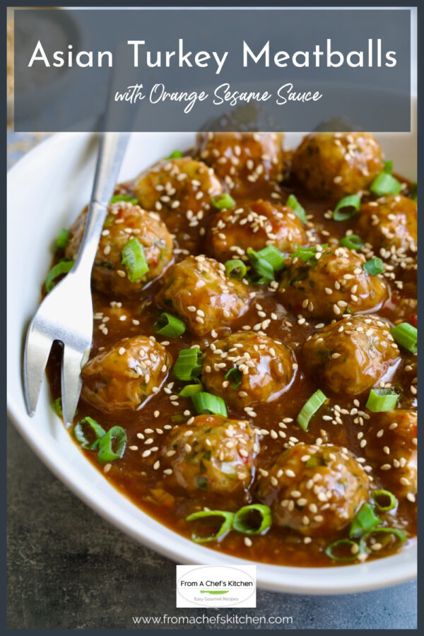 Asian Turkey Meatballs in white oval serving dish with serving fork garnished with sesame seeds and scallions.