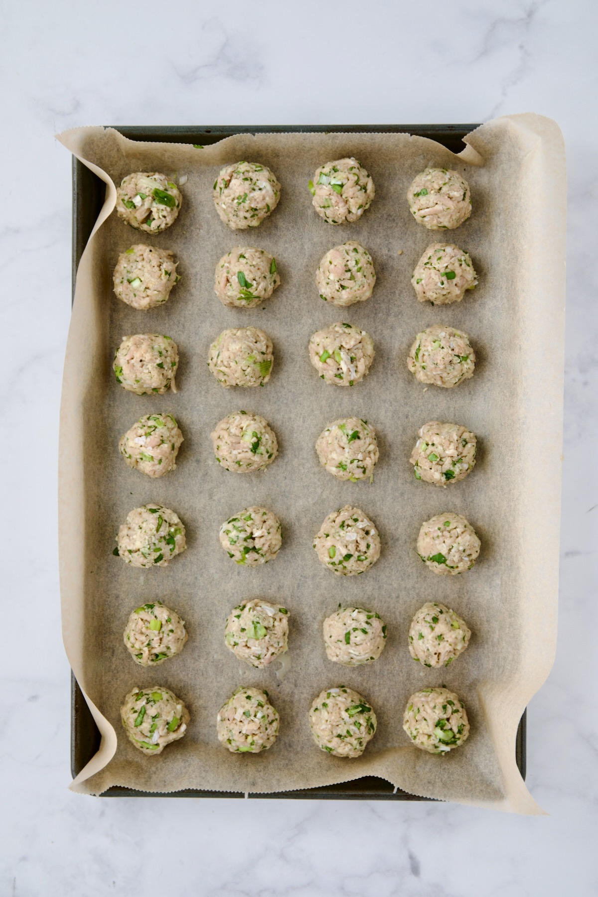 Turkey meatballs on parchment paper lined baking sheet before being baked.