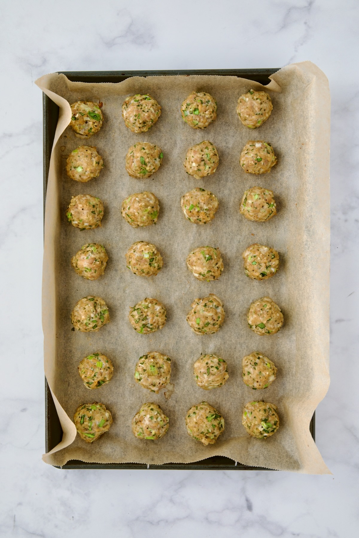 Turkey meatballs on parchment paper lined baking sheet after being baked.