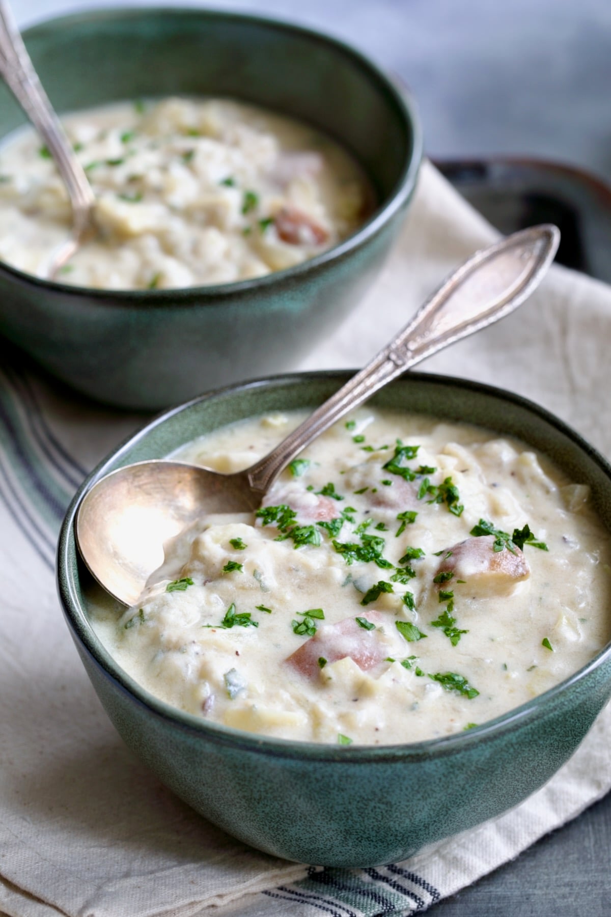 Two bowls of Creamy Potato Soup on striped towel with two soup spoons.