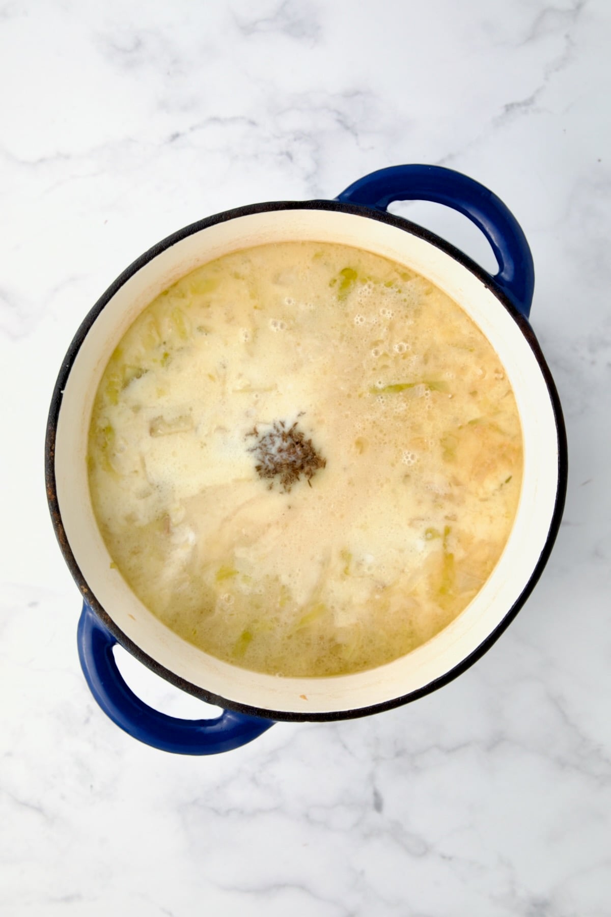 Caraway, Worcestershire and hot sauce added to soup in blue cast iron Dutch oven.