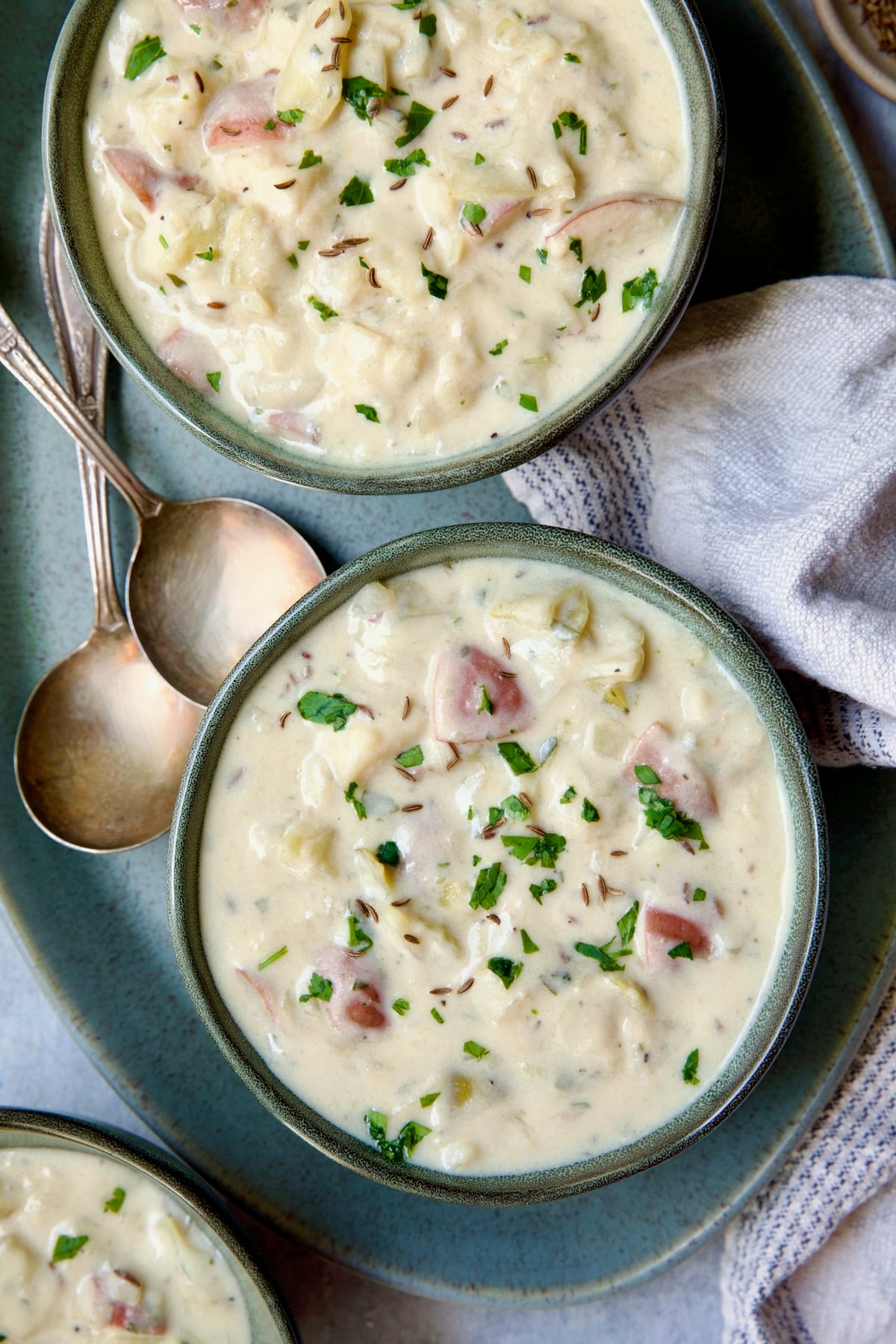 Two bowls of Creamy Potato Soup on green oval platter with two soup spoons.