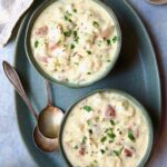 Two bowls of Creamy Potato Soup on green oval platter with two soup spoons.