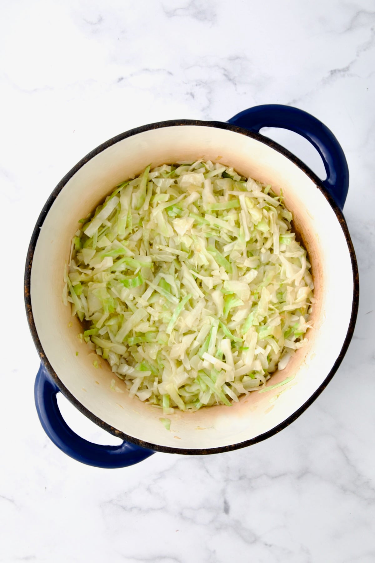 Uncooked cabbage added to cooked onions in blue cast iron Dutch oven.