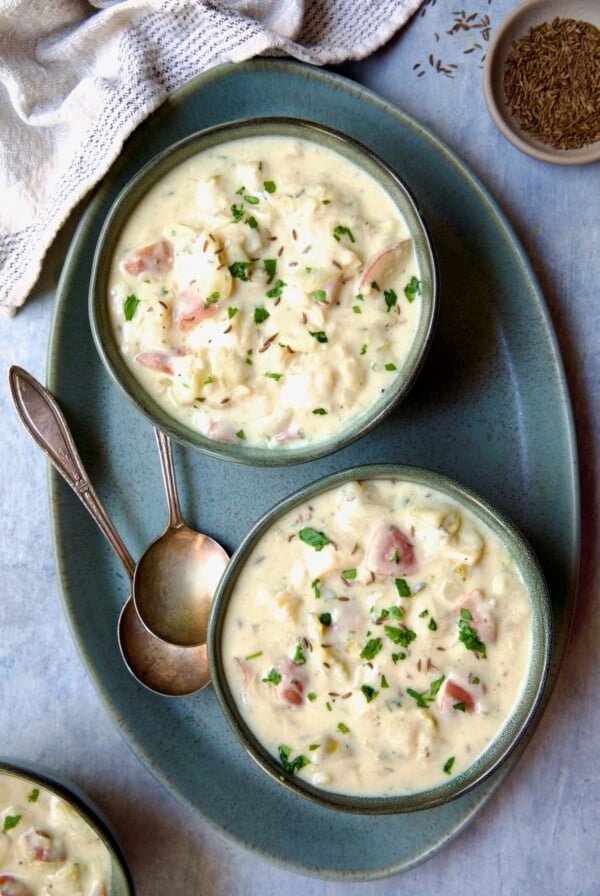 Two bowls of Creamy Potato Soup on green oval platter with two soup spoons.
