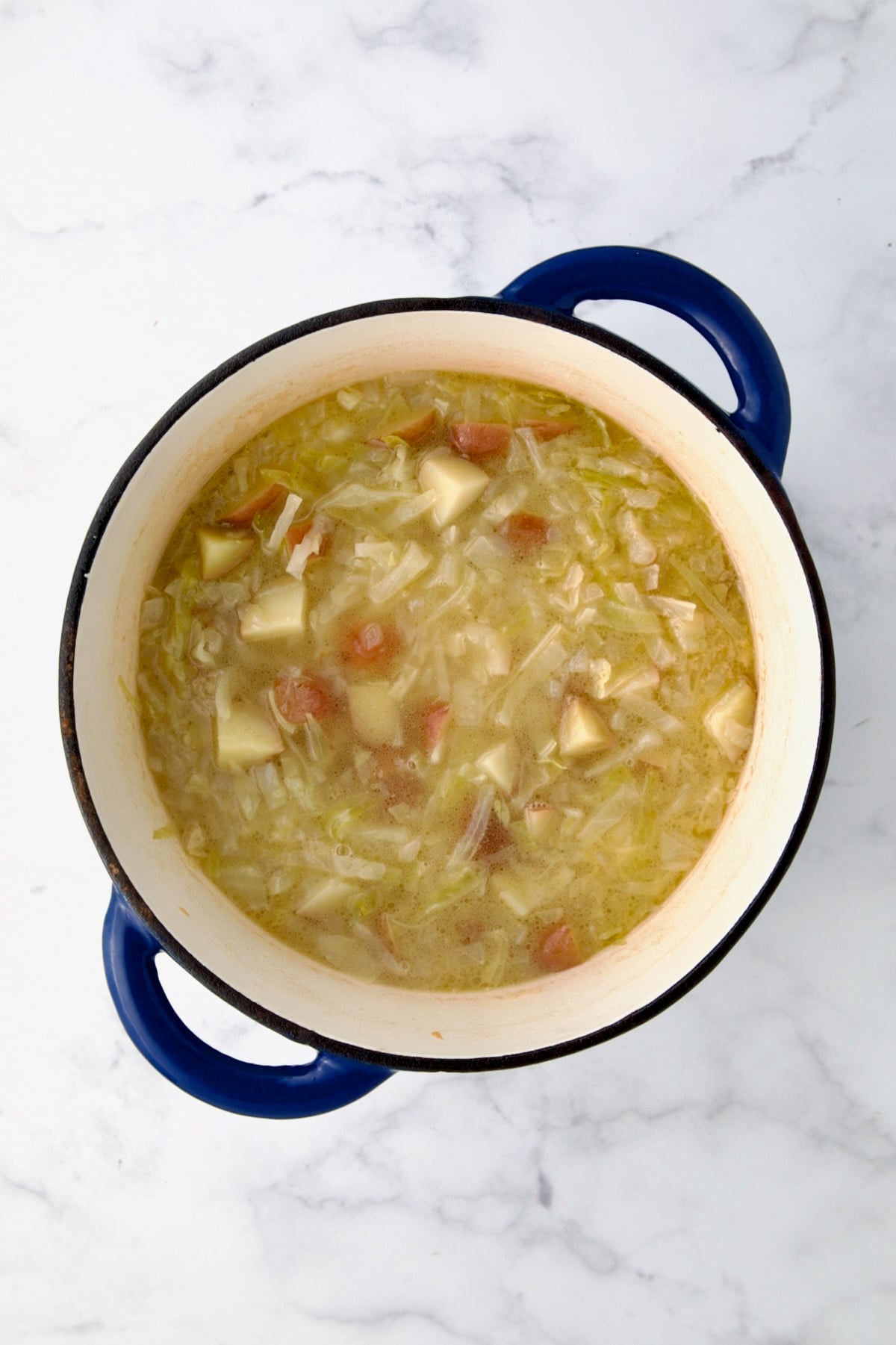 Chicken broth added to onions, cabbage and potatoes in blue cast iron Dutch oven.