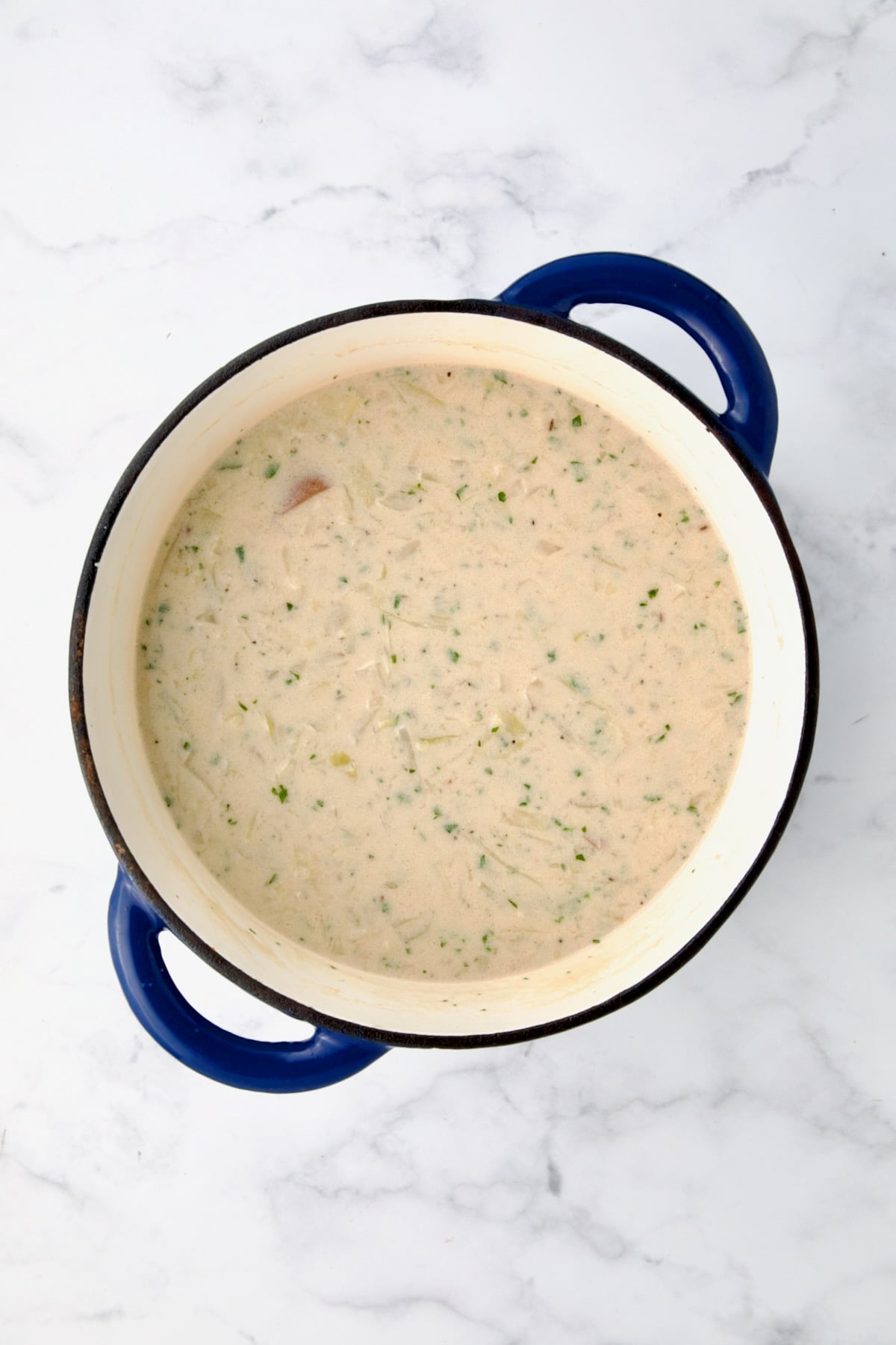 Thickened half-and-half and flour combination added to soup in blue cast iron Dutch oven.