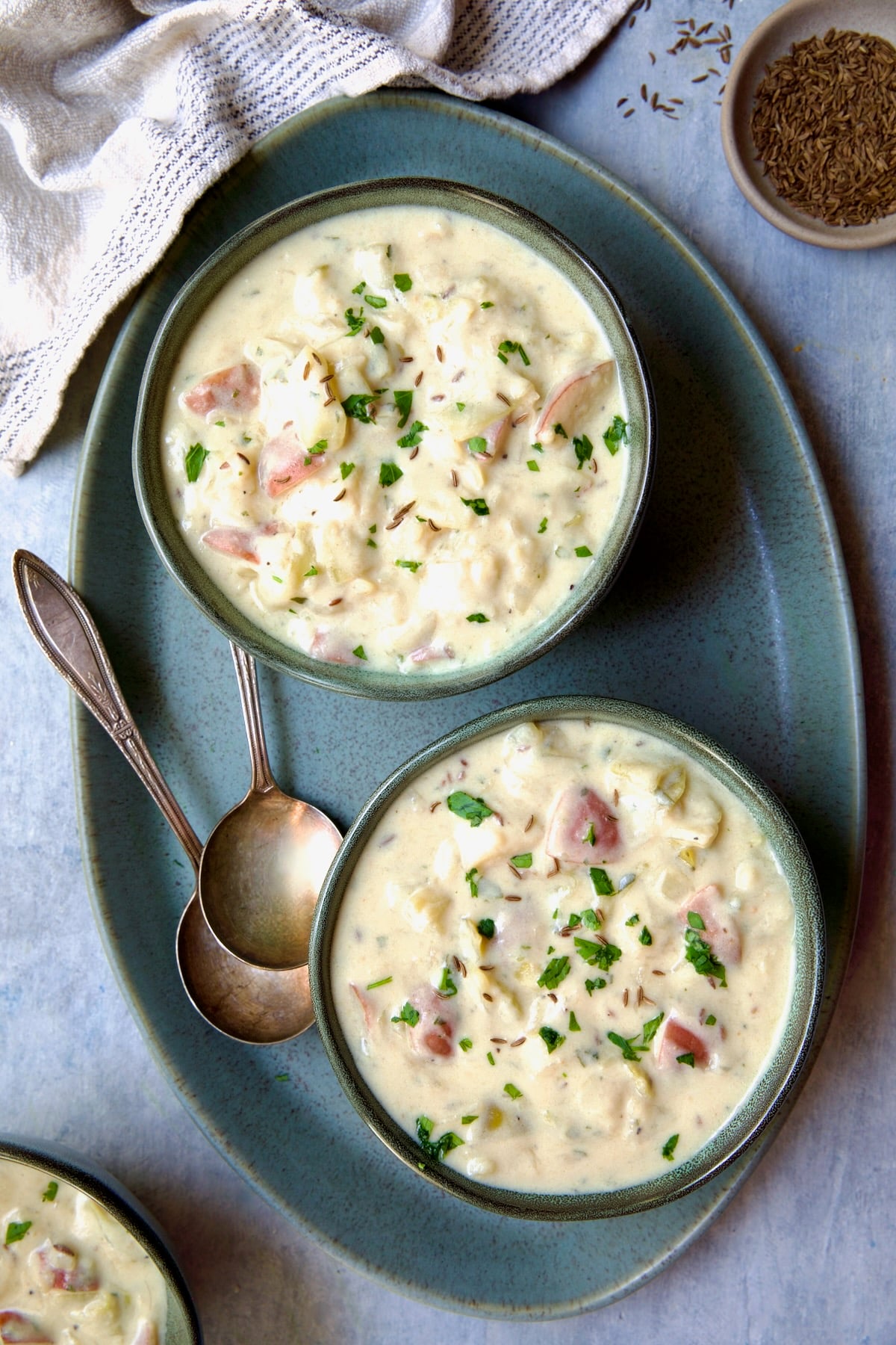 Two bowls of Creamy Potato Soup on green oval platter with two soup spoons.