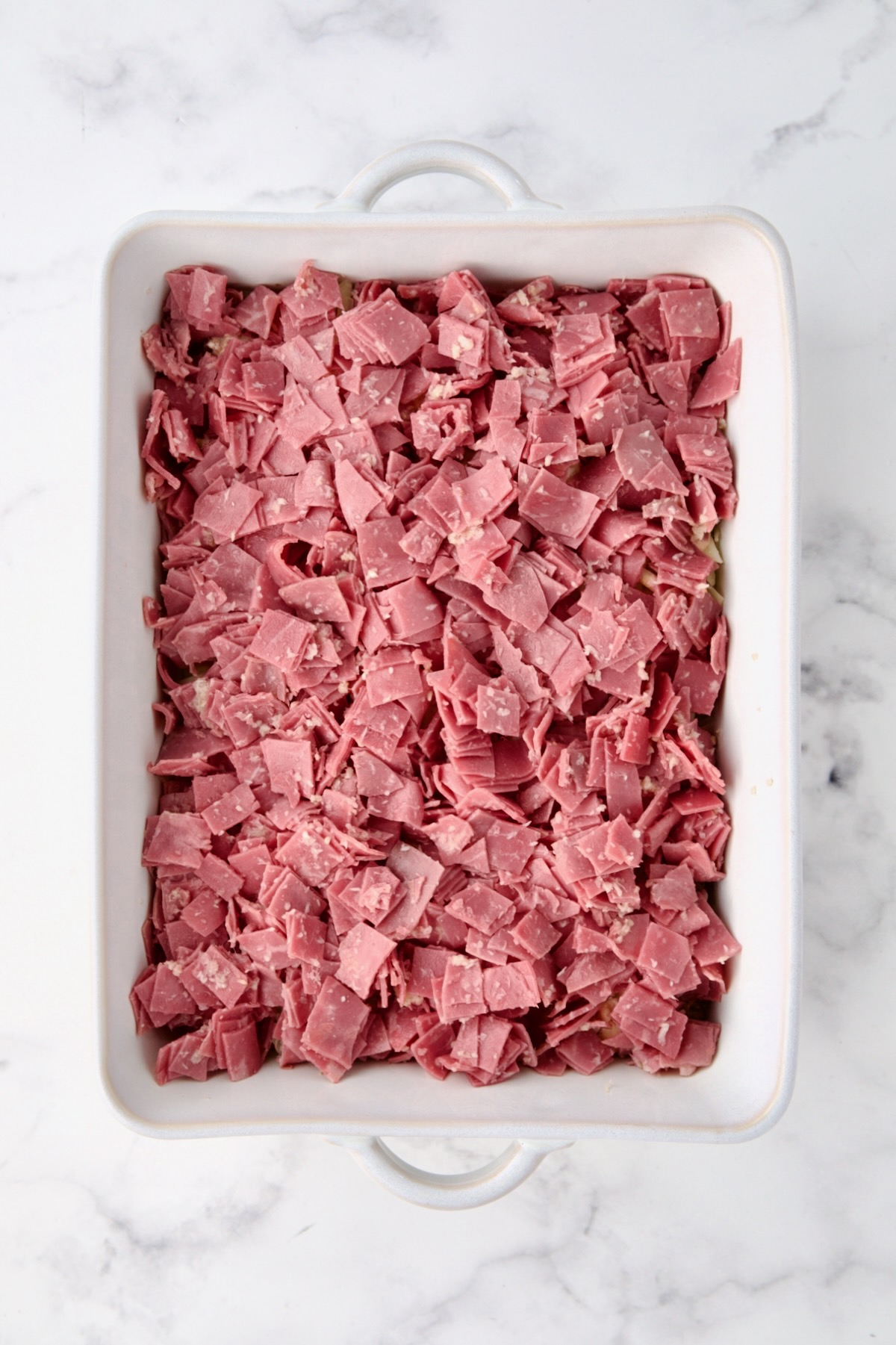 Corned beef placed over the other layers in white rectangular baking dish.