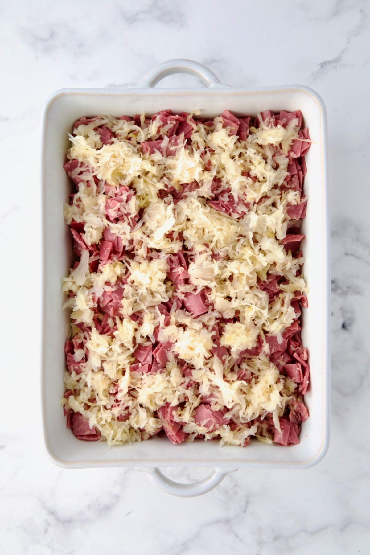 Sauerkraut on corned beef layer in white rectangular baking dish.