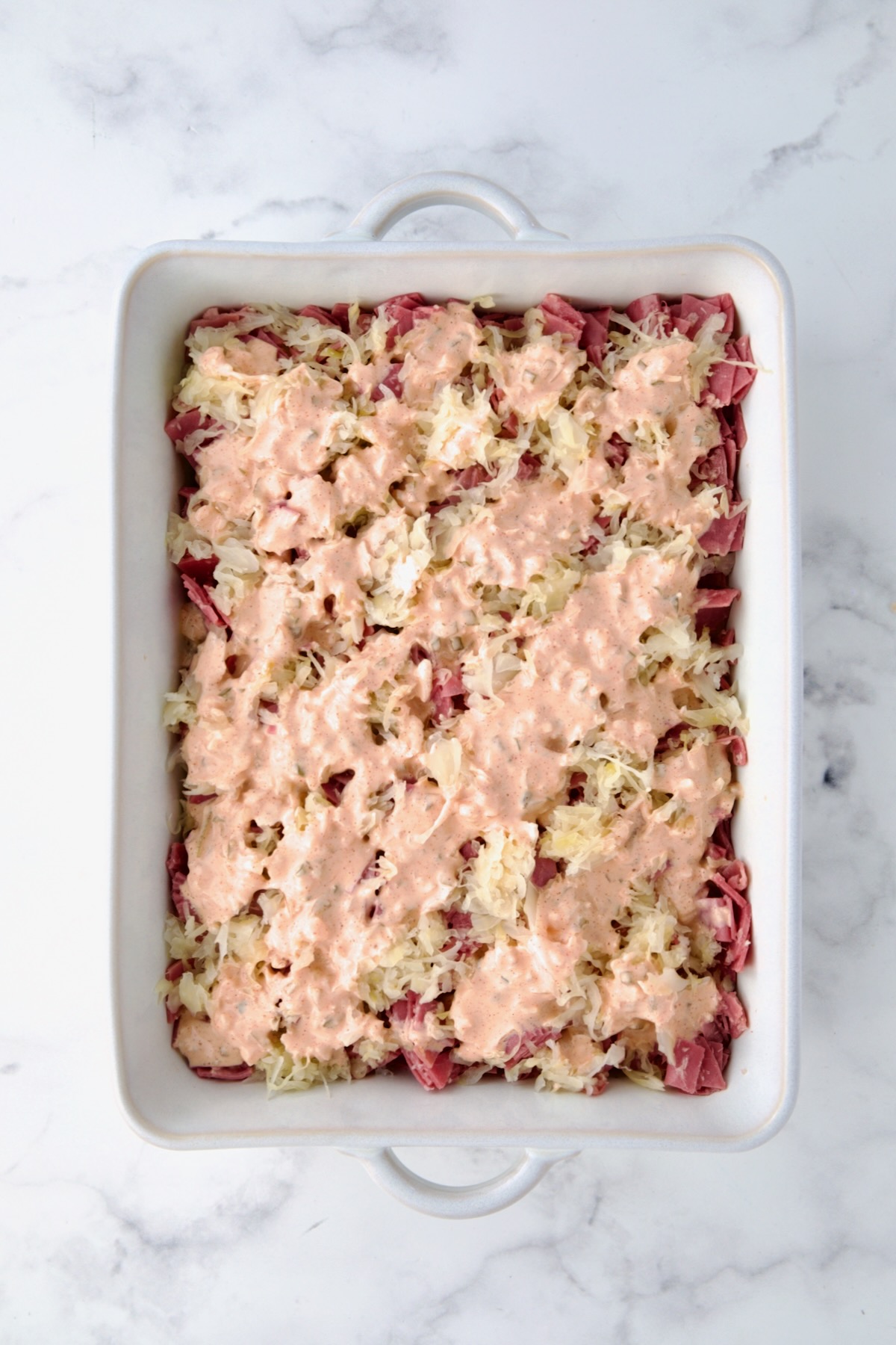 Thousand Island dressing over second sauerkraut layer in white rectangular baking dish.