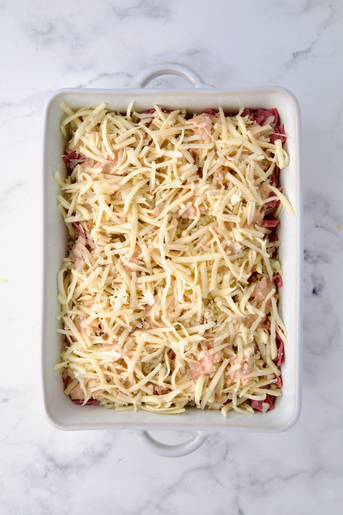 Final cheese layer on Reuben Casserole in white rectangular baking dish.