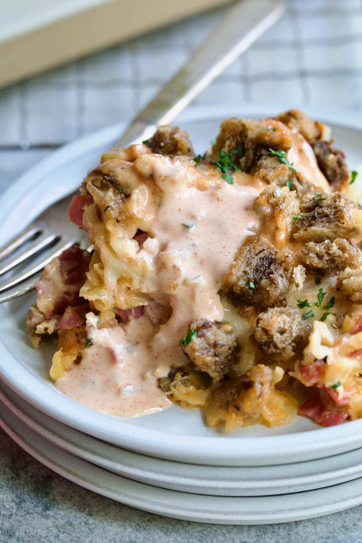 One serving of Reuben Casserole with serving spoon on white plate with fork drizzled with Thousand Island dressing.