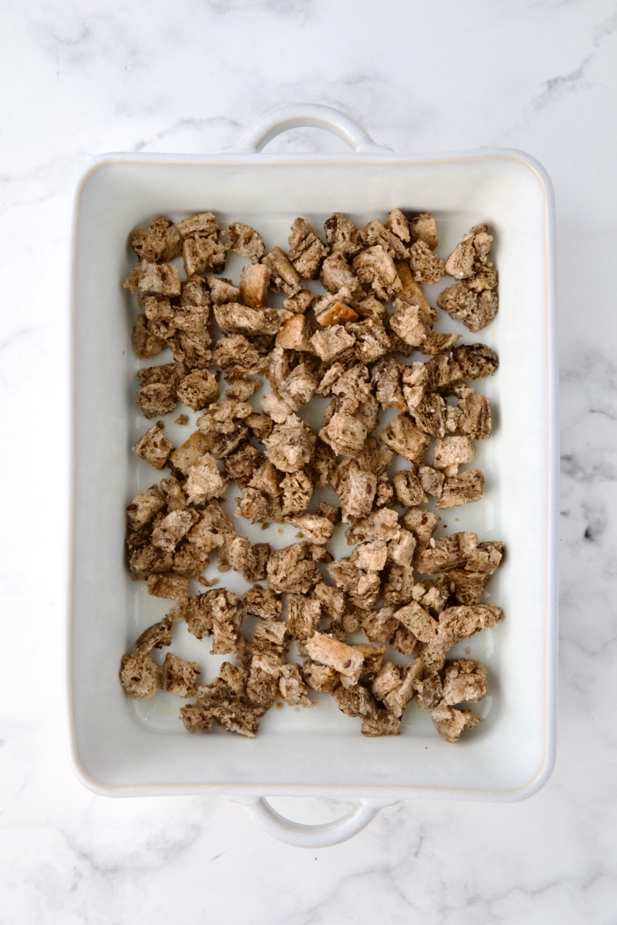 Rye bread cubes in white rectangular baking dish.