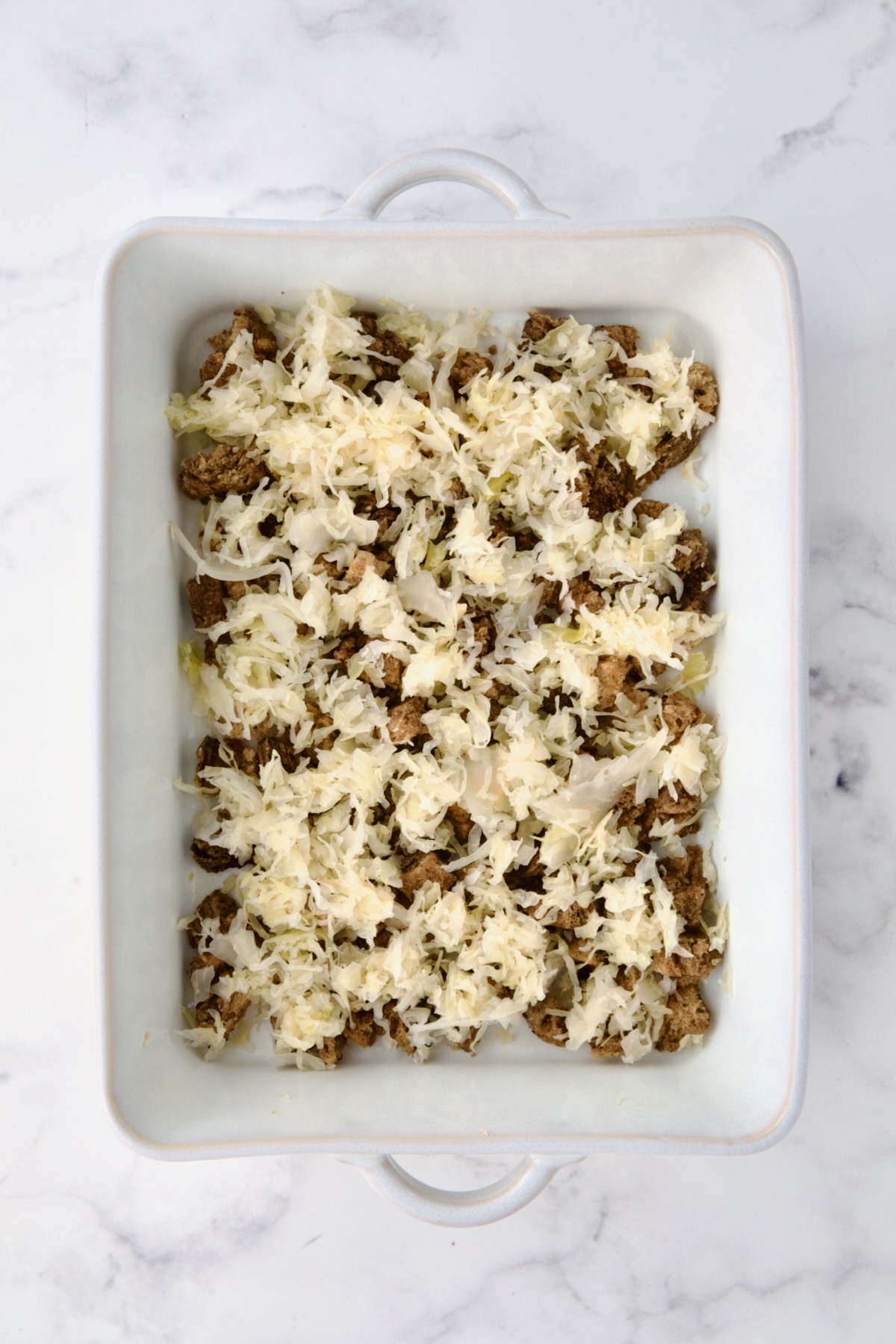 Sauerkraut placed over rye bread cubes in white rectangular baking dish.