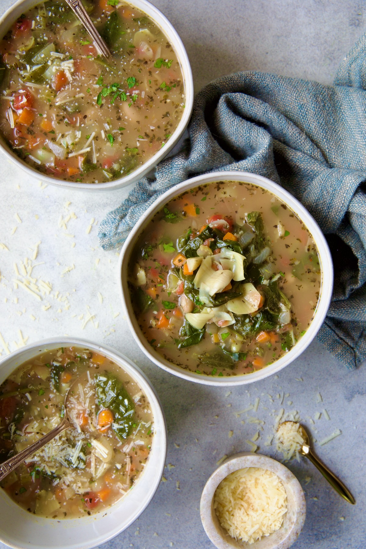 Three bowls of soup with light blue napkin and parmesan cheese sprinkled on the top.