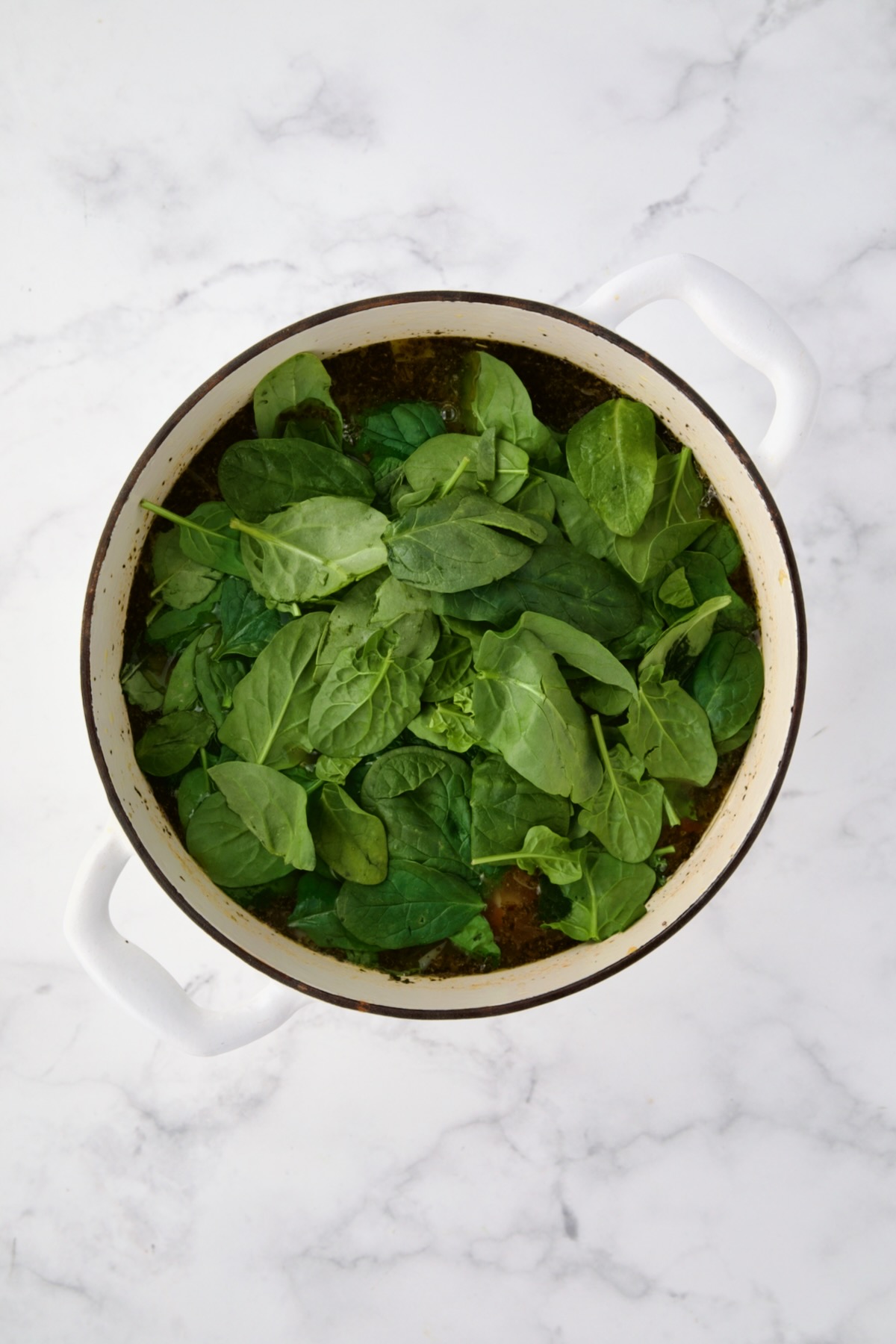 Spinach added to Vegetable Bean Soup in white Dutch oven.