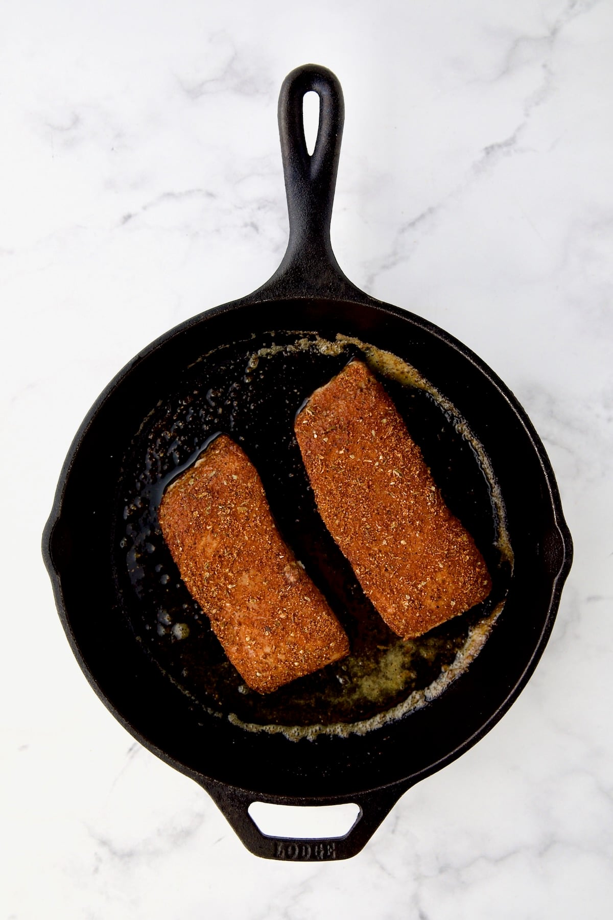 Two pieces of halibut coated with blackening seasoning in cast iron skillet.