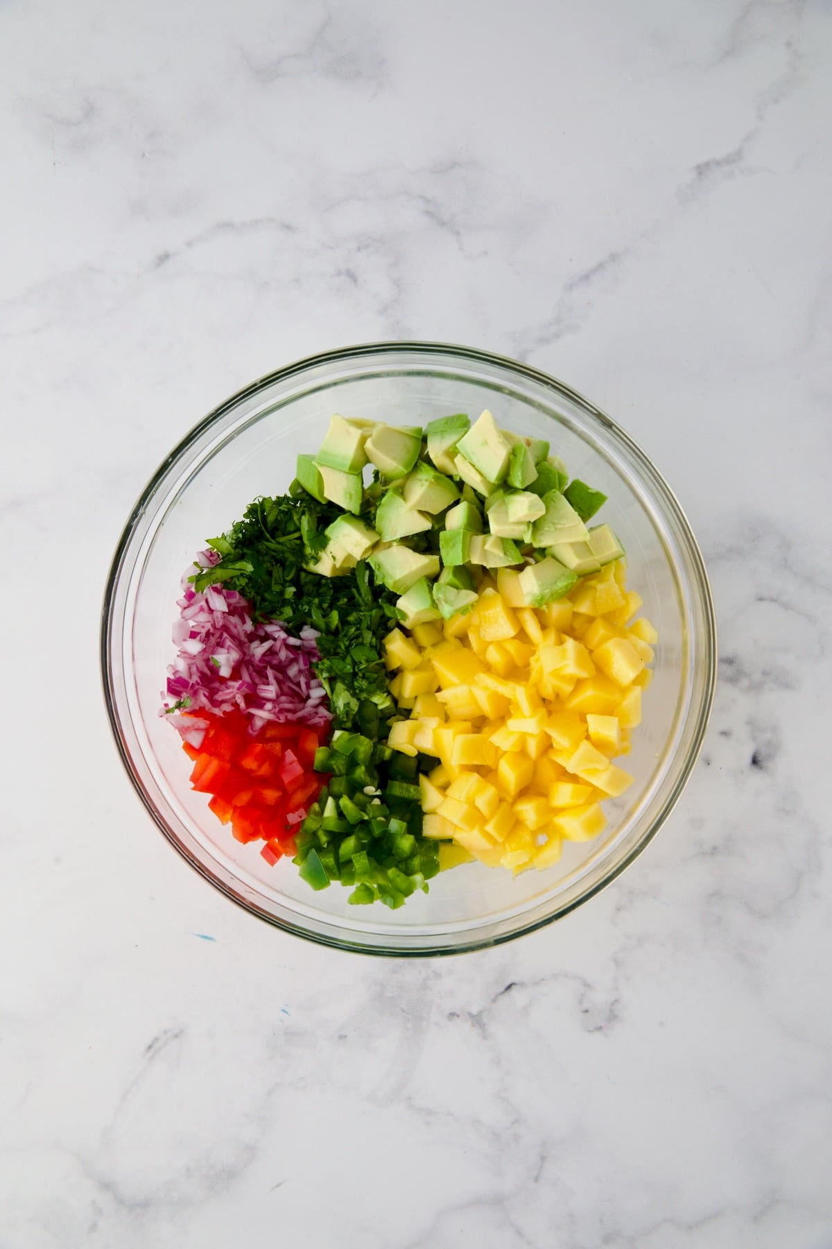 Ingredients for mango and avocado salsa in glass bowl before being stirred together.