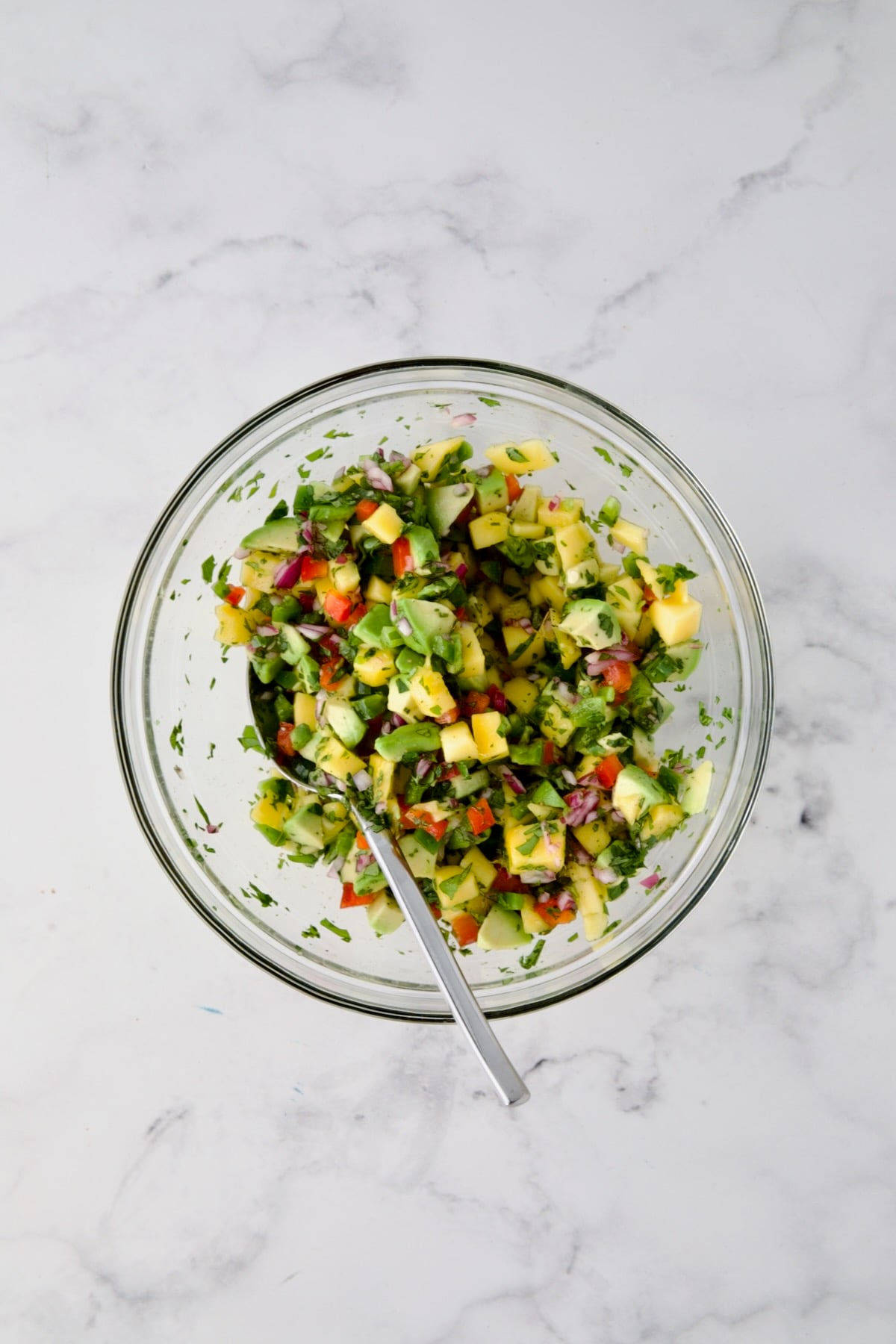 Ingredients for mango and avocado salsa in glass bowl after being stirred together with spoon.
