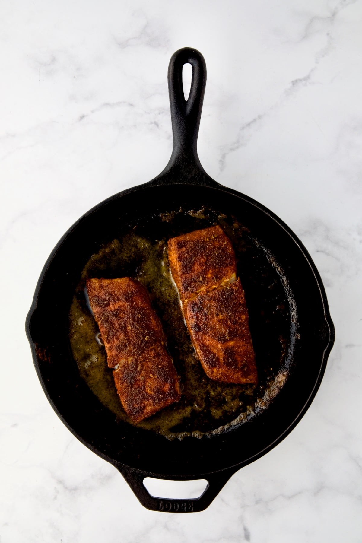 Two pieces of halibut coated with blackening seasoning in cast iron skillet after being cooked.