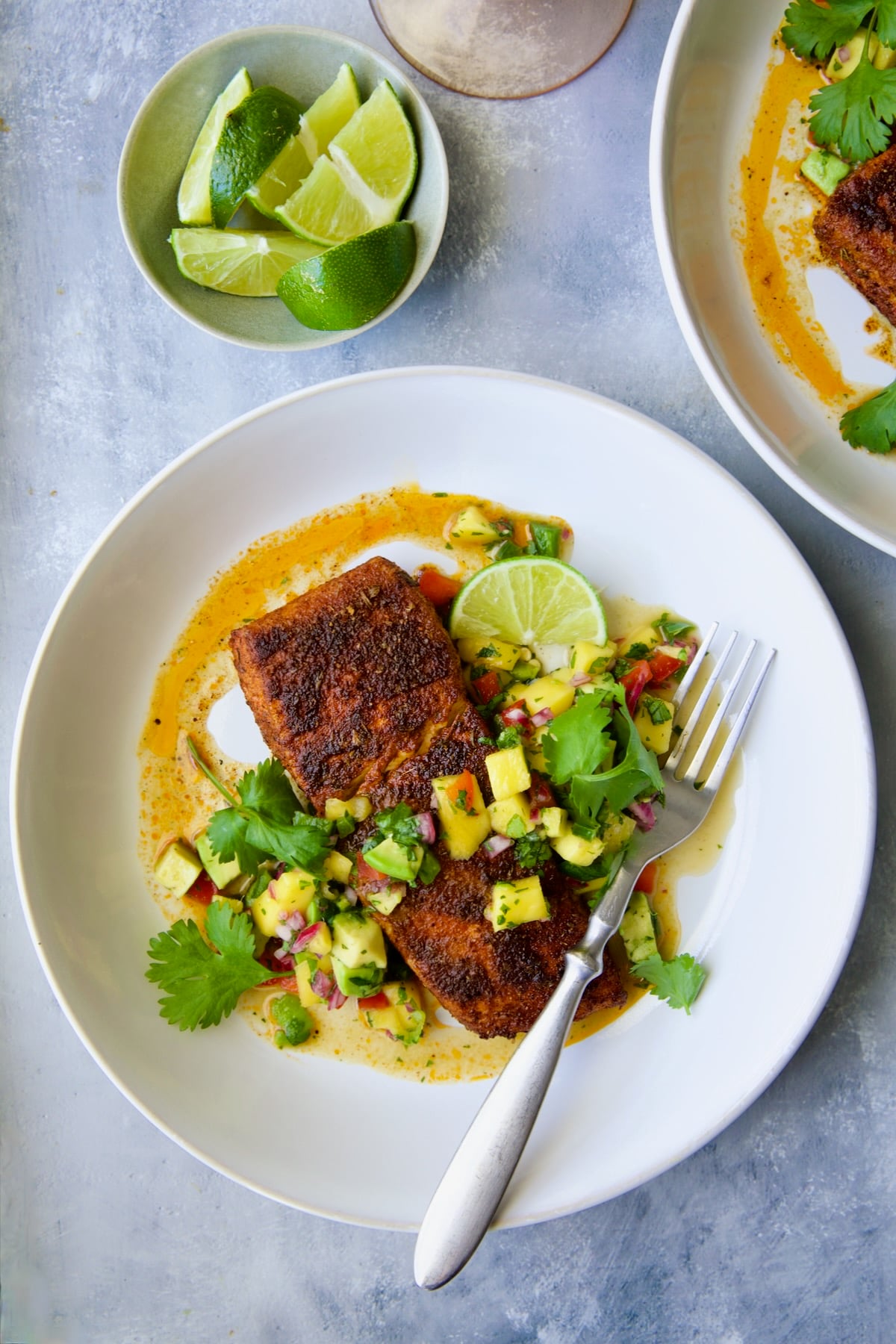 Blackened Halibut with Mango - Avocado Salsa on white plate with fork garnished with cilantro and lime wedge.