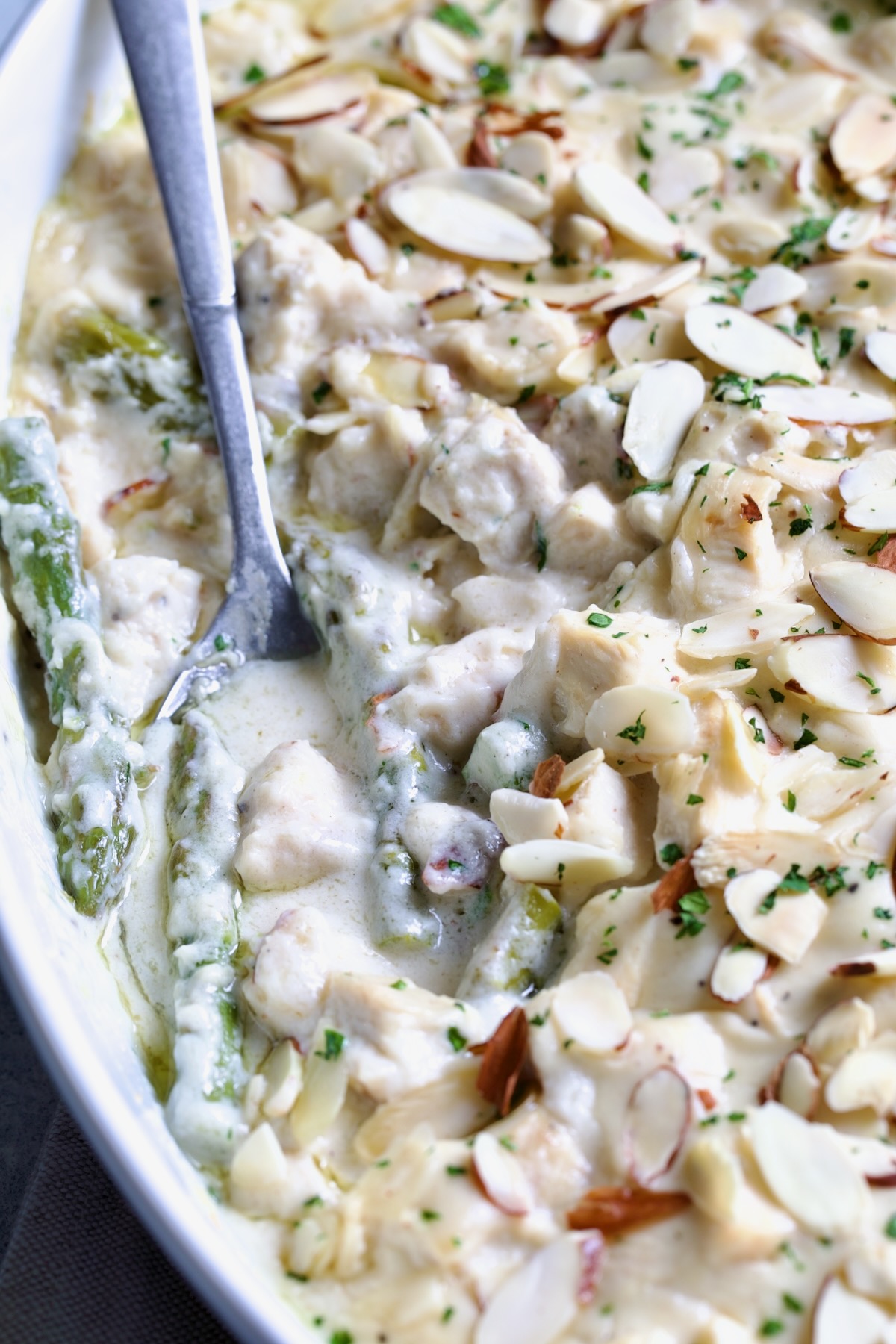 Chicken Divan with Asparagus in oval baking dish garnished with sliced almonds with serving spoon scooping some up.