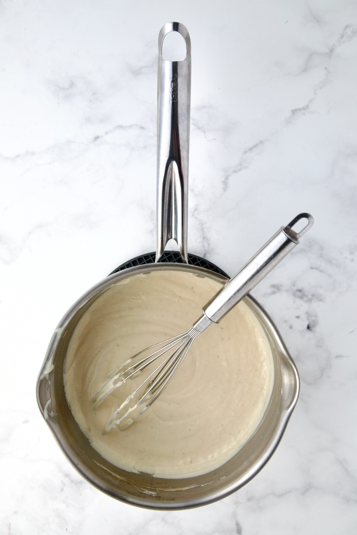 Thickened finished cheese sauce and wire whisk in stainless steel saucepan.