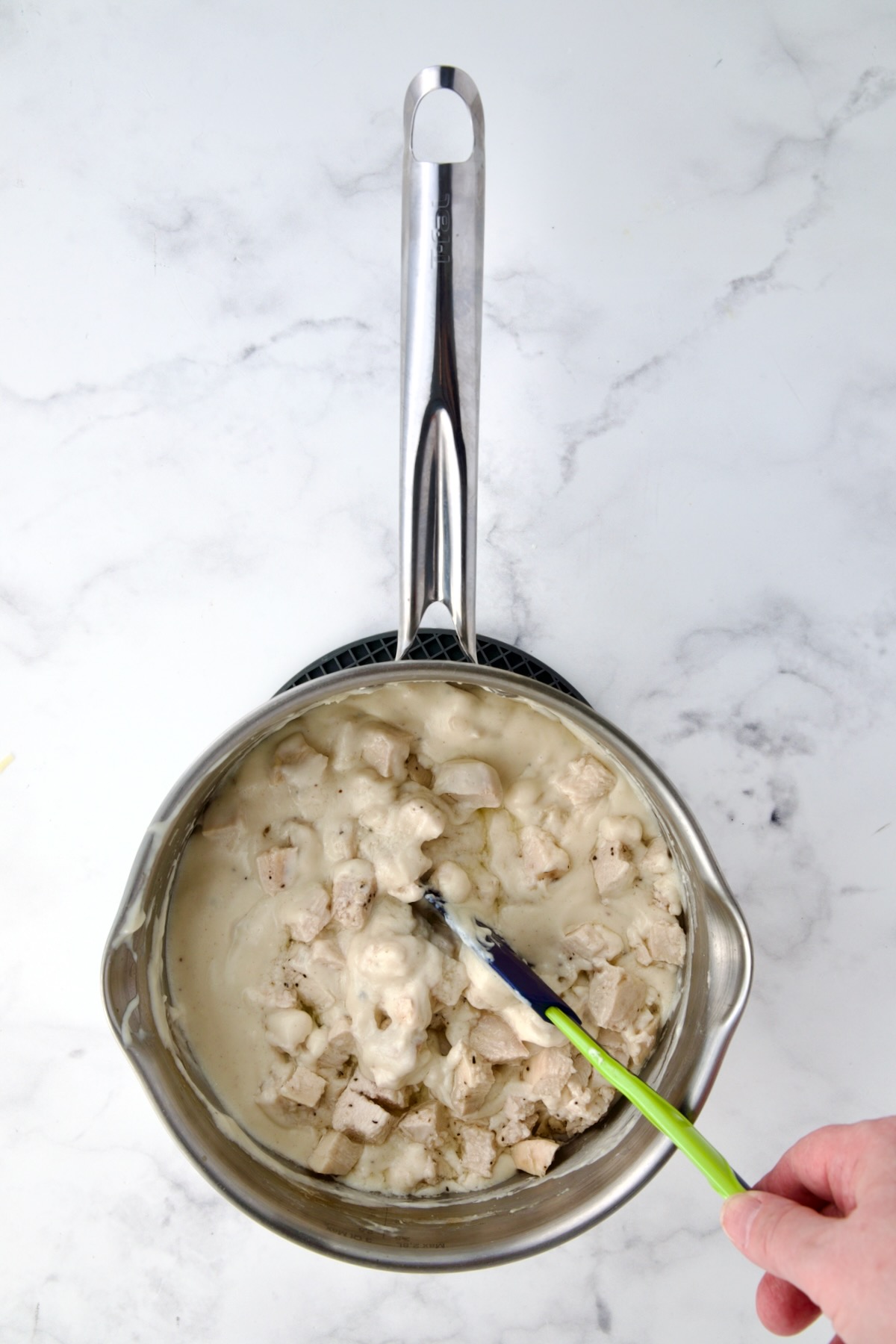 Chicken being stirred into cheese sauce with spatula.