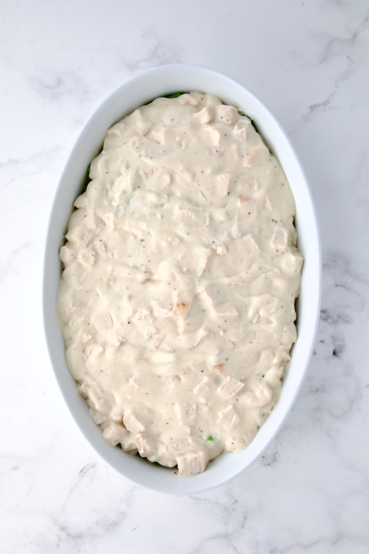 Cheese sauce with diced chicken poured over the top of blanched asparagus in oval baking dish.