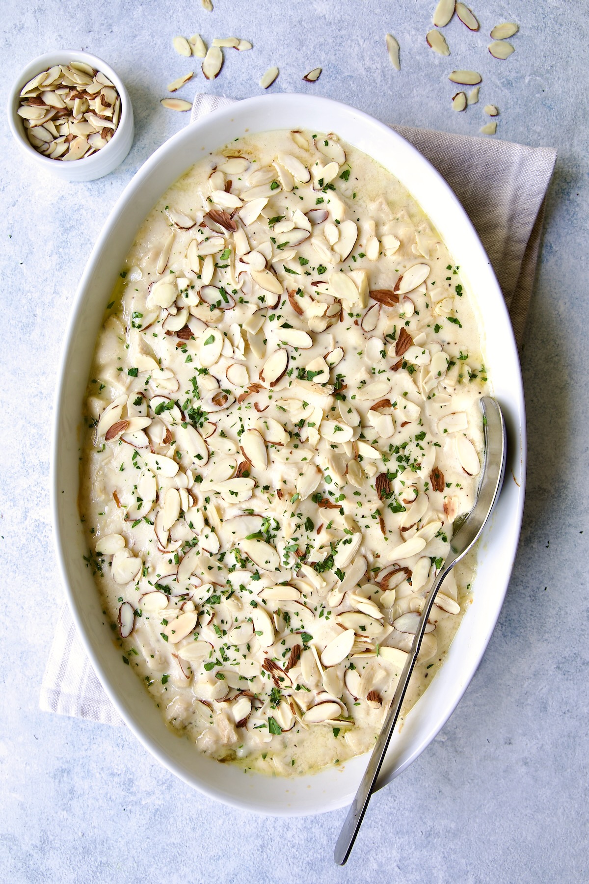 Chicken Divan with Asparagus in oval baking dish with serving spoon garnished with sliced almonds.