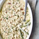 Chicken Divan with Asparagus in oval baking dish with serving spoon garnished with sliced almonds with asparagus and chicken exposed.