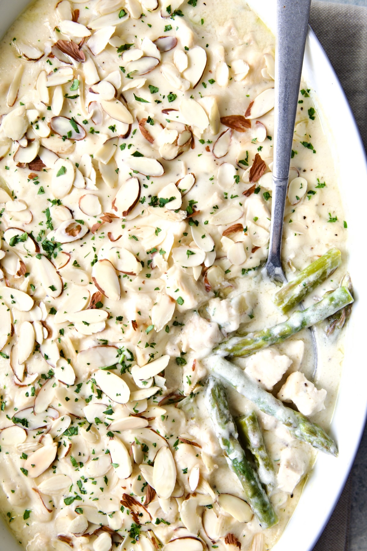 Chicken Divan with Asparagus in oval baking dish garnished with sliced almonds with serving spoon scooping some up.