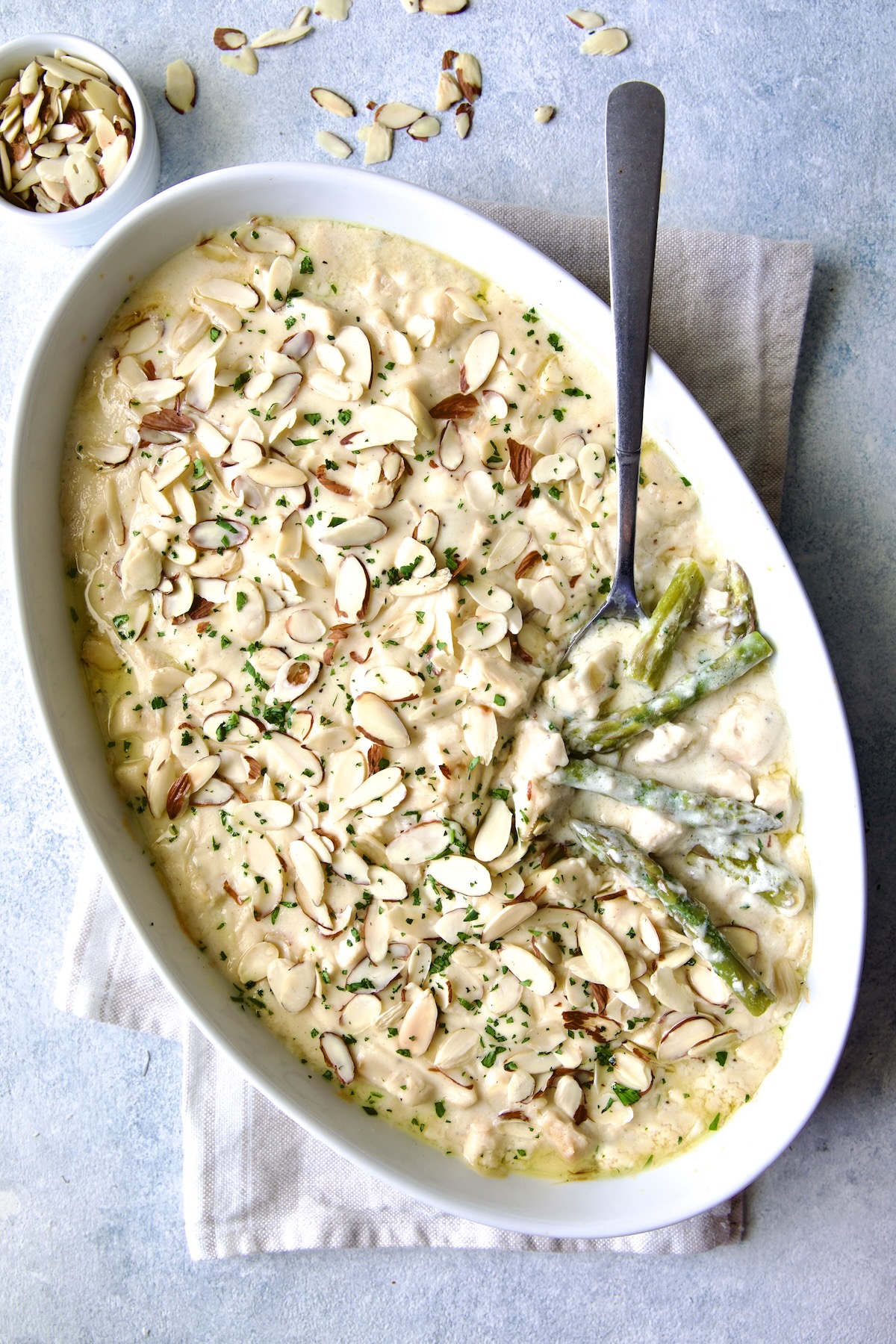 Chicken Divan with Asparagus in oval baking dish with serving spoon garnished with sliced almonds with asparagus and chicken exposed.