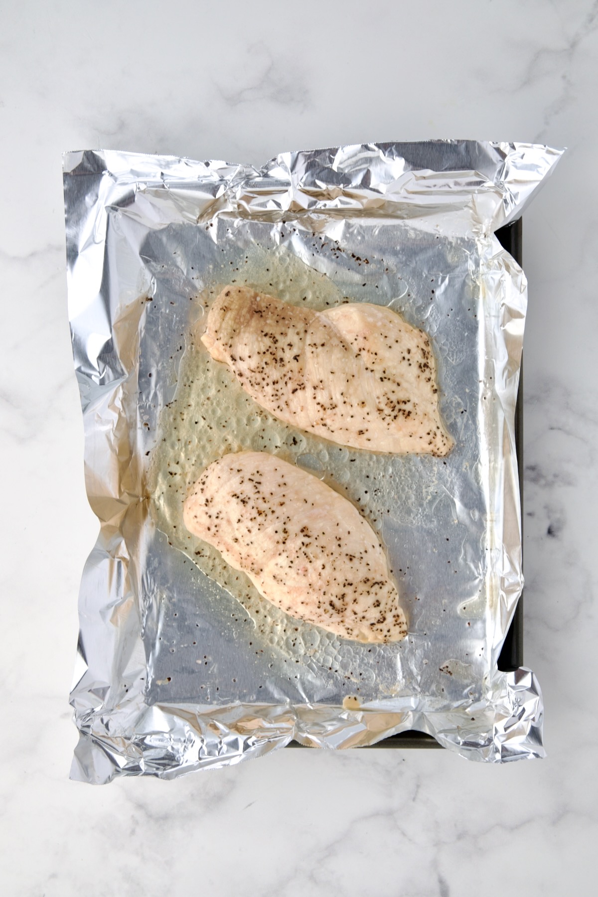 Two cooked chicken breasts on aluminum foil lined baking sheet.
