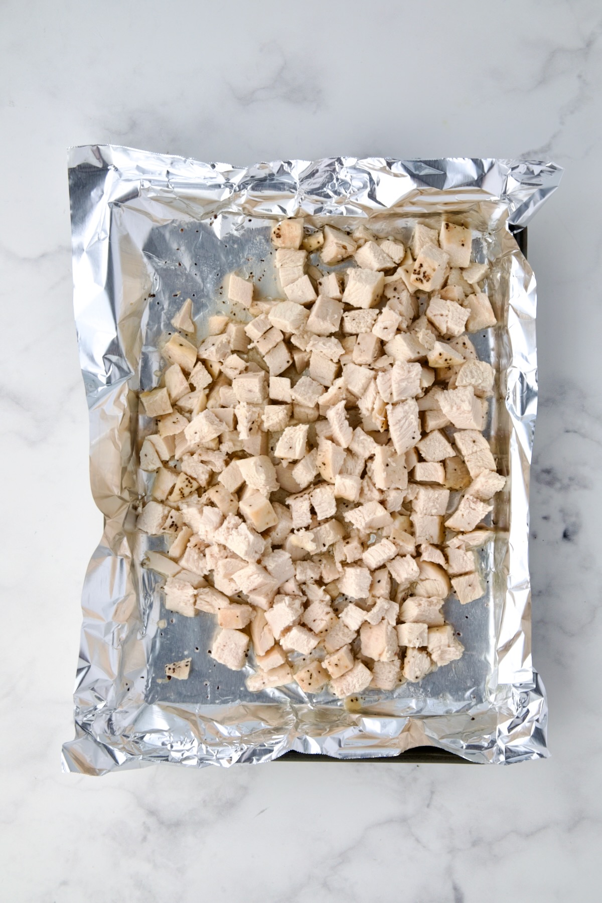 Cubed chicken on aluminum foil-lined baking sheet.