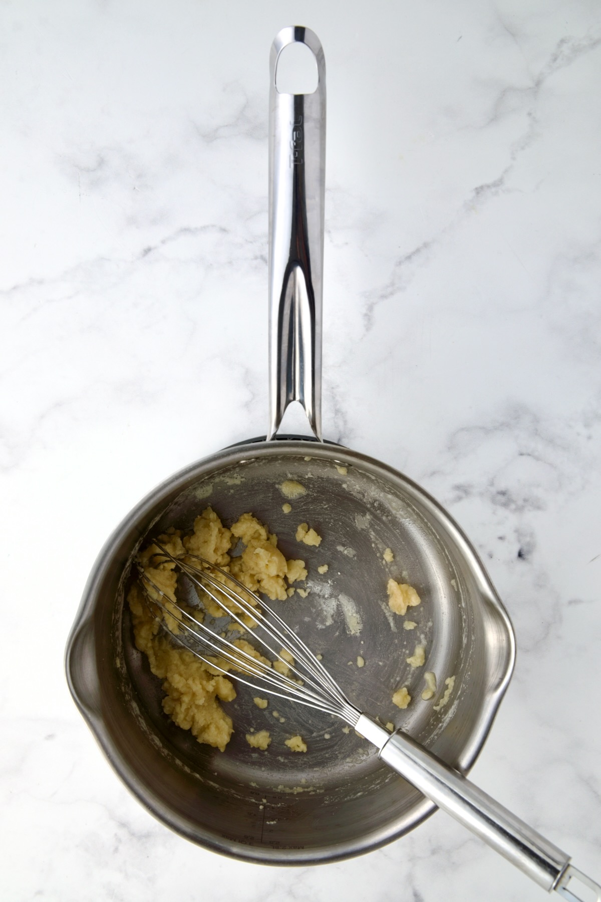 Butter and flour being whisked in stainless steel saucepan.