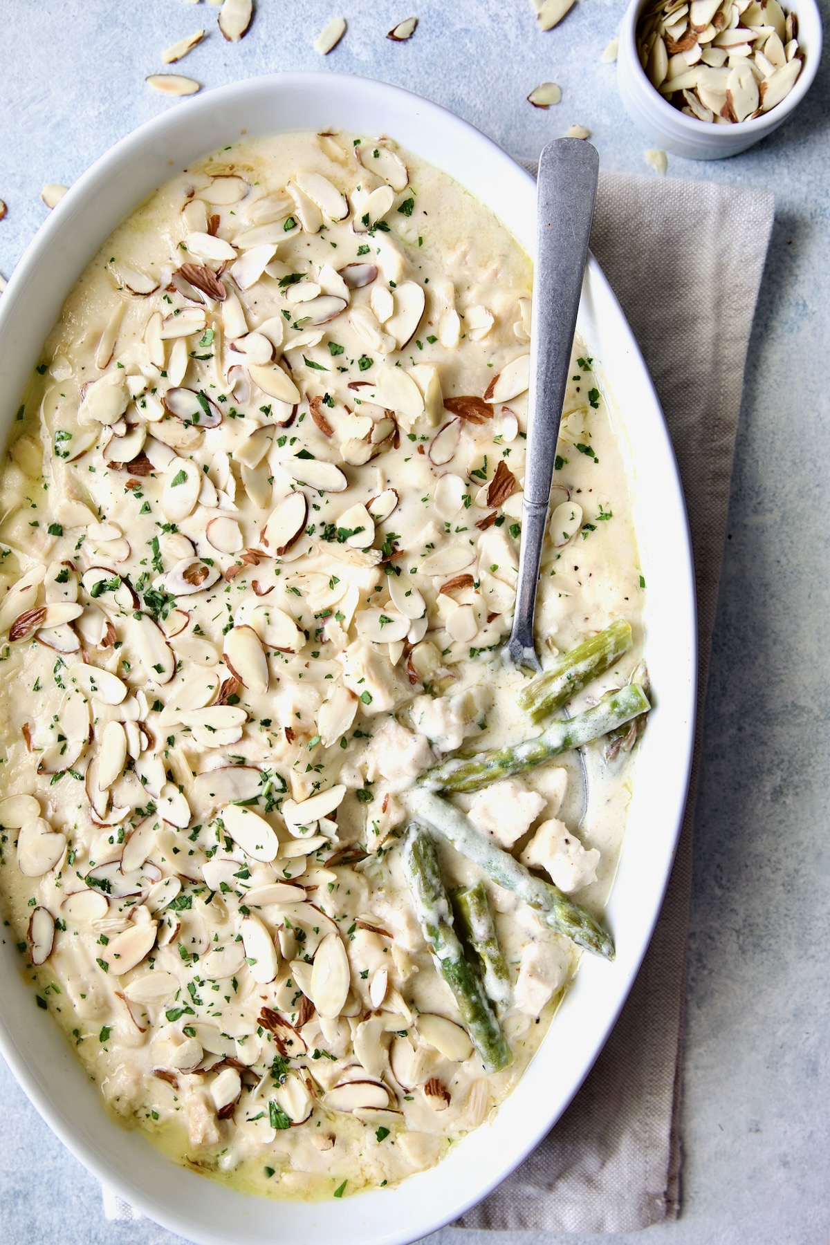 Chicken Divan with Asparagus in oval baking dish with serving spoon garnished with sliced almonds with asparagus and chicken exposed.
