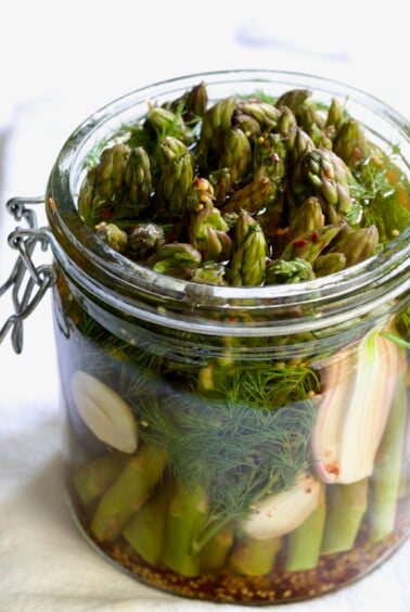 Asparagus with brine poured over it in glass jar.