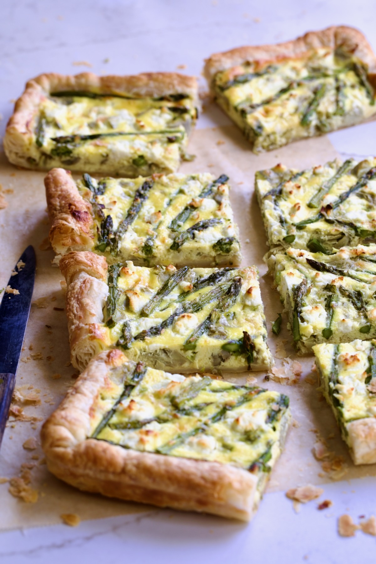 Eight pieces of Puff Pastry Vegetable Tart on brown parchment paper with knife nearby.
