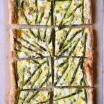 Puff Pastry Vegetable Tart on brown parchment paper cut into eight pieces with knife nearby.
